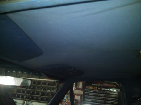 1993 Ford Bronco - The interior ceiling of a vehicle is visible, including sun visors and a reflection in the rearview mirror showing shelves and tools.