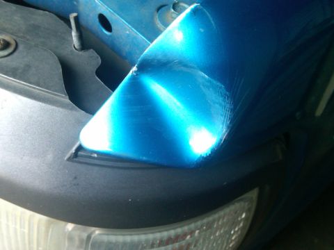 1993 Ford Bronco - The corner of a blue fender shows significant damage and scratches.