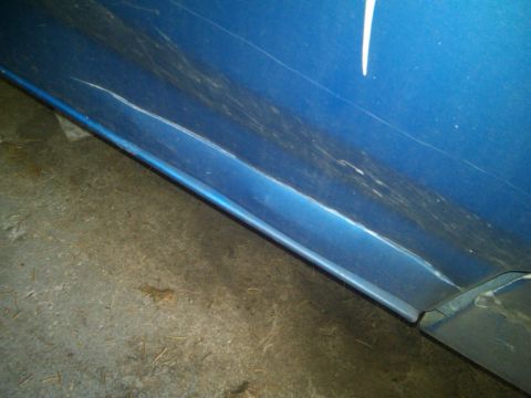 1993 Ford Bronco - Close-up of a damaged blue vehicle door, showing scuffs and a noticeable crease near the bottom edge.