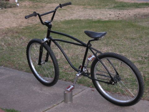 1994 Ford Bronco - A black bicycle with a custom frame and wide handlebars is shown parked on a sidewalk next to a grassy area.
