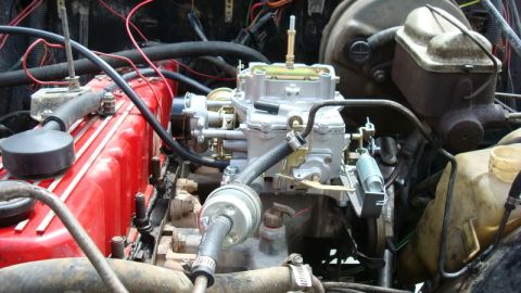 1982 Jeep Wagoneer - The engine bay features a prominent carburetor and a red valve cover, surrounded by a complex network of wires and hoses.