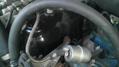 1982 Jeep Wagoneer - Close-up view of an engine bay, a black valve cover and a silver fuel filter. Text on a hose indicates a date.