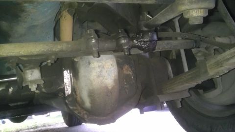 1982 Jeep Wagoneer - The underside of a vehicle shows a heavily corroded front axle and suspension components.