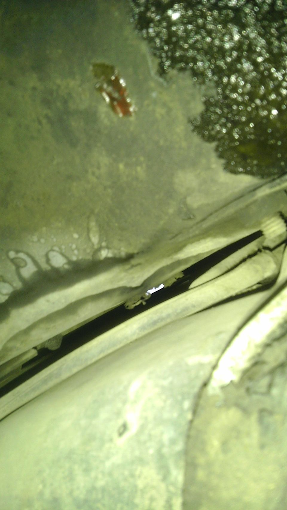 Underside of a vehicle with visible oil leaks and a dark, narrow channel