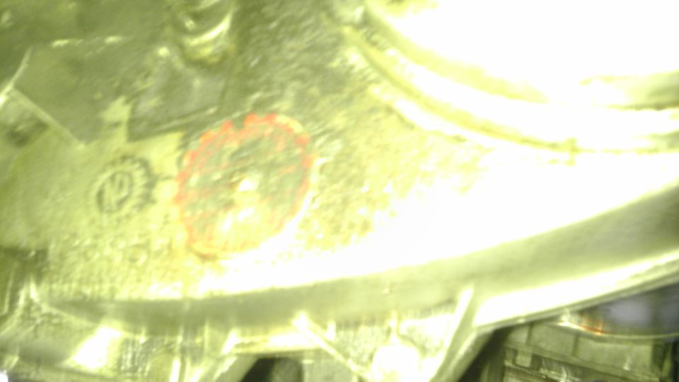 Close-up of a metal part with a red circular marking and some stamped letters