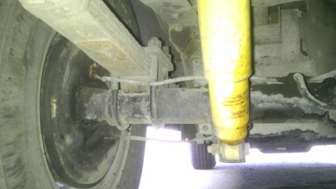 1982 Jeep Wagoneer - Close-up view of the rear suspension and axle assembly of a vehicle, showing the leaf springs and a yellow shock absorber.