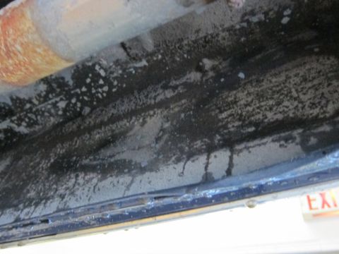 1991 Ford LTD Crown Victoria - Close-up of a vehicle's frame rail, showing corrosion and dirt. An exit sign is partially visible.