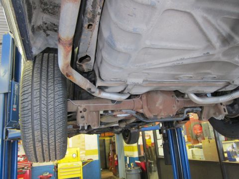 1991 Ford LTD Crown Victoria - The undercarriage of a vehicle is shown while it is raised on a hydraulic lift for inspection.