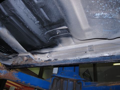 1991 Ford LTD Crown Victoria - The undercarriage of a vehicle is shown, with visible rust on the frame and some black protective coating.