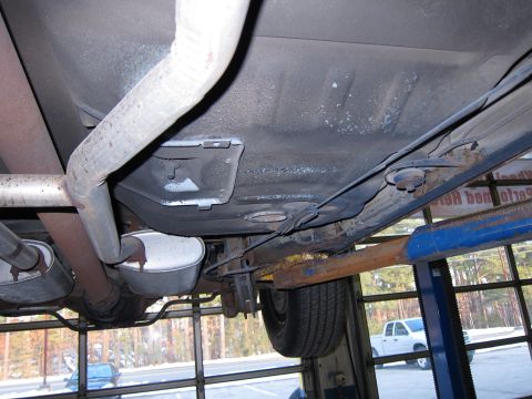 1991 Ford LTD Crown Victoria - The underside of a vehicle is shown on a lift, with a white pickup truck visible through the garage door in the background.