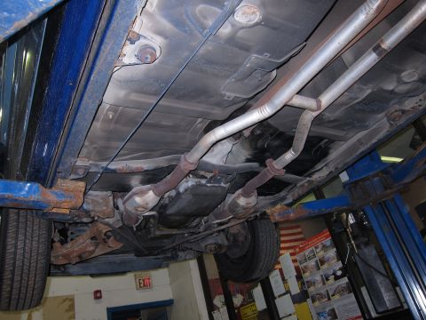 1991 Ford LTD Crown Victoria - The undercarriage of a vehicle is shown on a lift, revealing its exhaust system and suspension components.