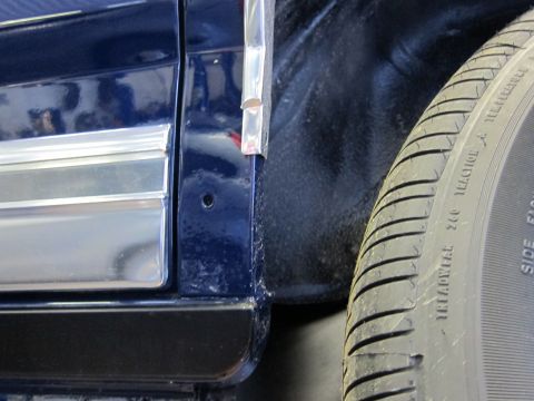1991 Ford LTD Crown Victoria - Close-up of a dark blue car's side panel and tire, showing chrome trim and tire sidewall markings.