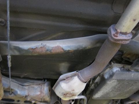 1991 Ford LTD Crown Victoria - The underside of a vehicle displays significant rust on the frame and exhaust system components.