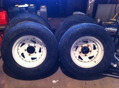 1994 Ford Bronco - Four tires with white rims are stacked in a garage setting.