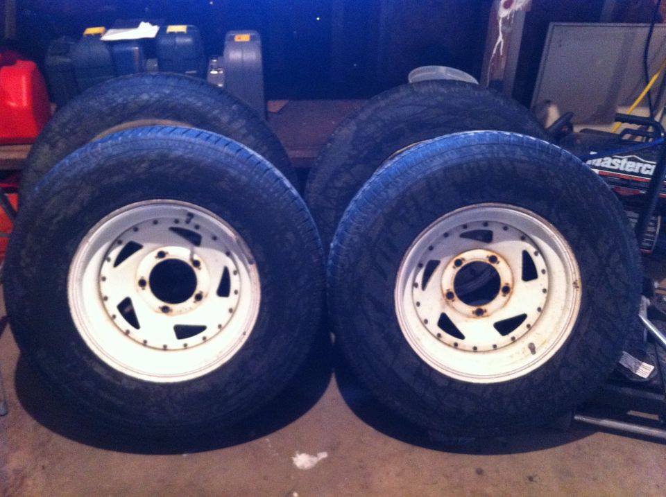 Four tires with white rims stacked in a garage