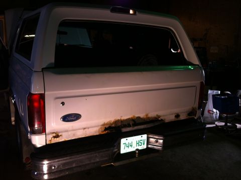 1994 Ford Bronco - The rear of a white SUV, possibly a Ford Bronco, shows significant rust around the tailgate and bumper.