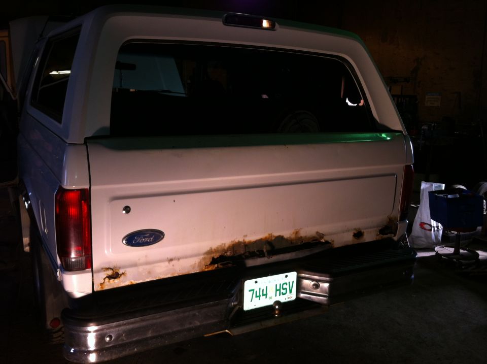Rear view of white SUV with green stripe and rusty tailgate