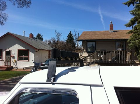 1994 Ford Bronco - A white SUV's roof is visible with a cargo rack overhead, set against a backdrop of houses and a clear blue sky.