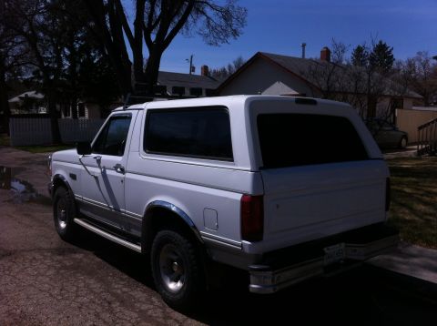 1994 Ford Bronco - This white SUV is shown from the rear 3/4 angle, a roof rack and chrome trim.