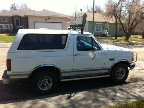 1994 Ford Bronco - A white Ford Bronco is parked on a residential street under a clear sky.