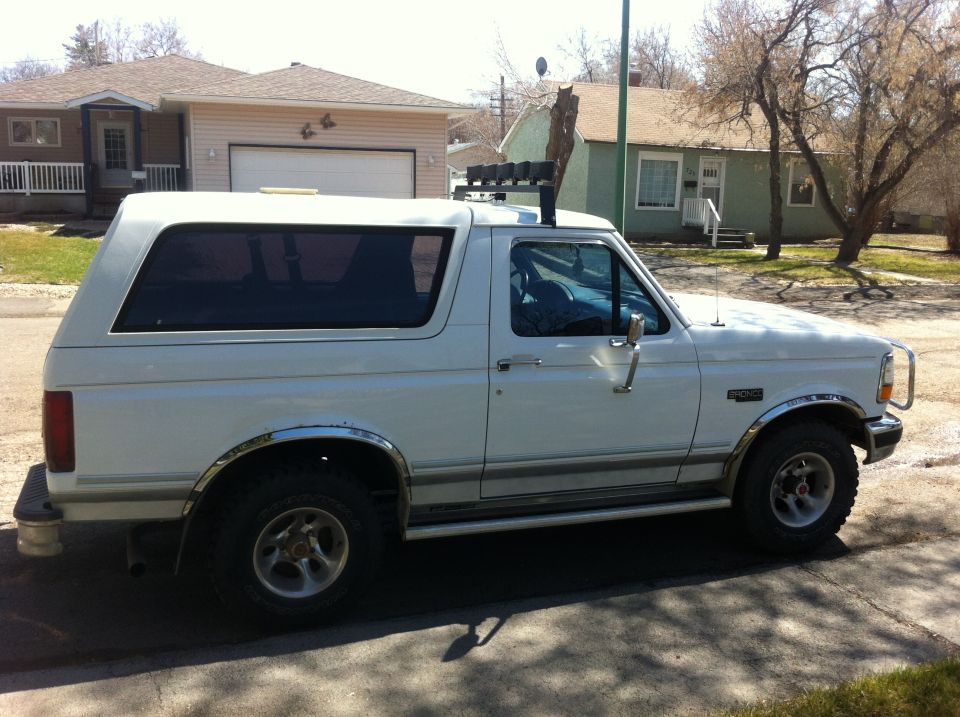 White 1994 Ford Bronco parked on street, side view. Has roof rack with lights