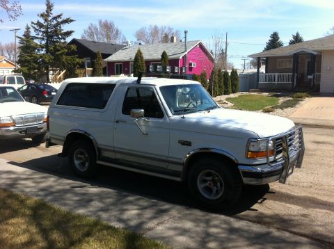 1994 Ford Bronco - A white Ford Bronco is parked on the side of the road in front of houses.