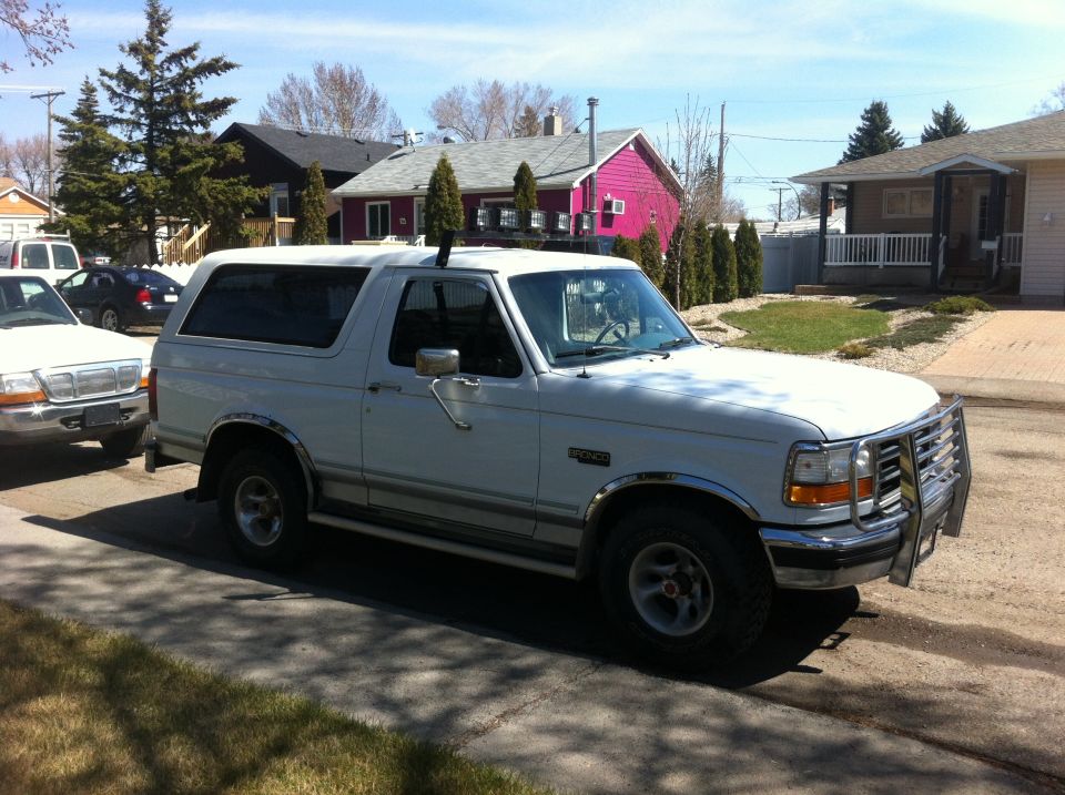 White Ford Bronco parked on a residential street, front 3/4 view. Bull bar on front