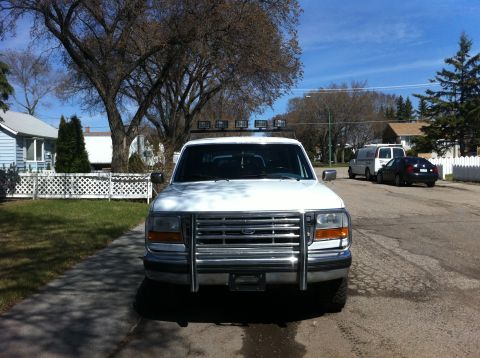1994 Ford Bronco - Front view of a white 1994 Ford Bronco, equipped with a chrome grille guard and auxiliary lights on the roof.