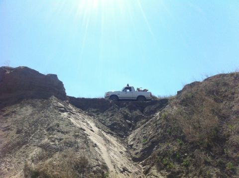 1994 Ford Bronco - A white pickup truck is parked on a ridge with a dirt bike in its bed, under a bright sunny sky.