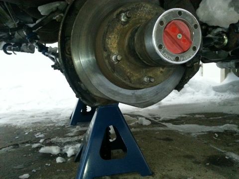 1994 Ford Bronco - Close-up of a vehicle's front wheel hub and brake rotor assembly, supported by blue jack stands in a snowy environment.