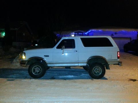 1994 Ford Bronco - A white 1994 Ford Bronco is parked on a snowy street at night, with house lights and blue Christmas lights visible in the background.