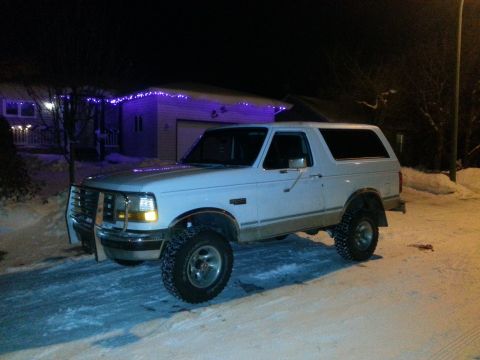 1994 Ford Bronco - A white Ford Bronco is parked outside a house decorated with purple lights on a snowy night.