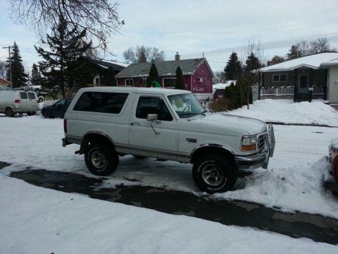 1994 Ford Bronco - A white Ford Bronco is parked on a snowy street in front of houses.