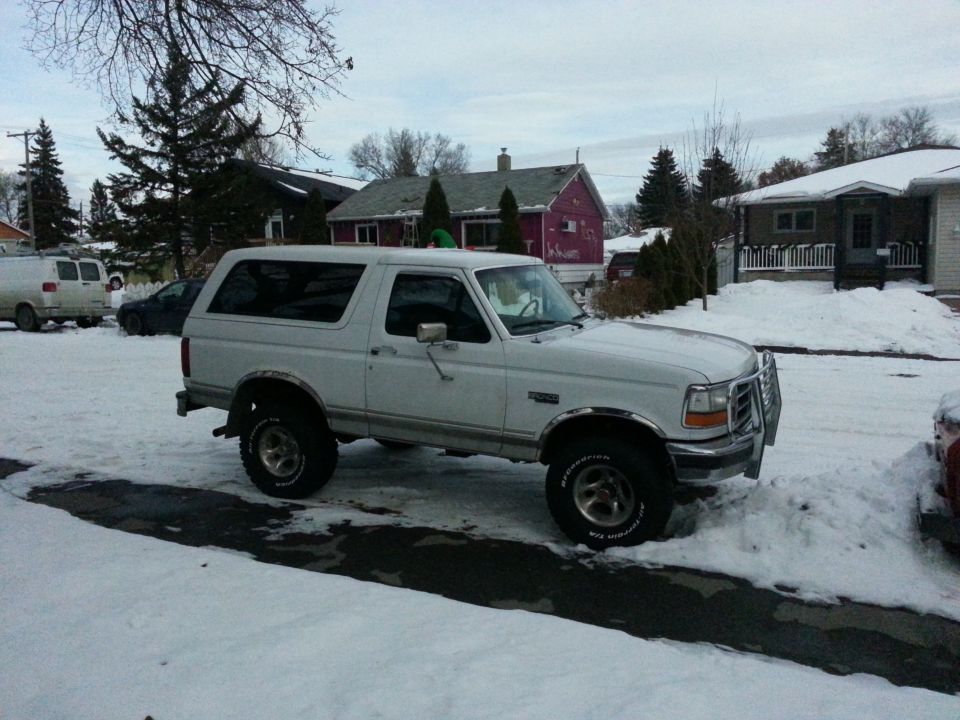 White Ford Bronco parked in snow, 3/4 front view. Chrome grille guard and fender trim visible