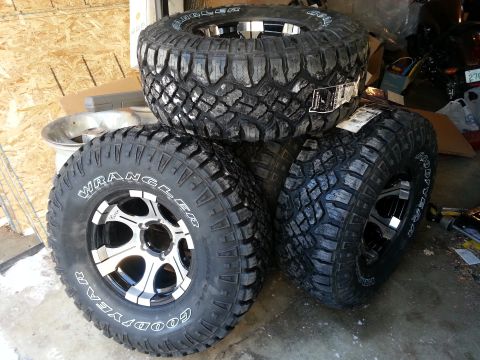 1994 Ford Bronco - A set of four Goodyear Wrangler off-road tires with custom rims are piled up in a garage setting.