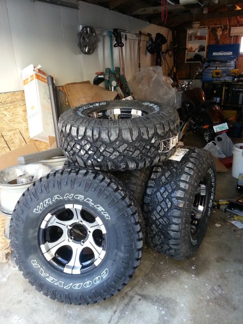 1994 Ford Bronco - Four Goodyear Wrangler off-road tires and wheels are stacked in a garage setting.