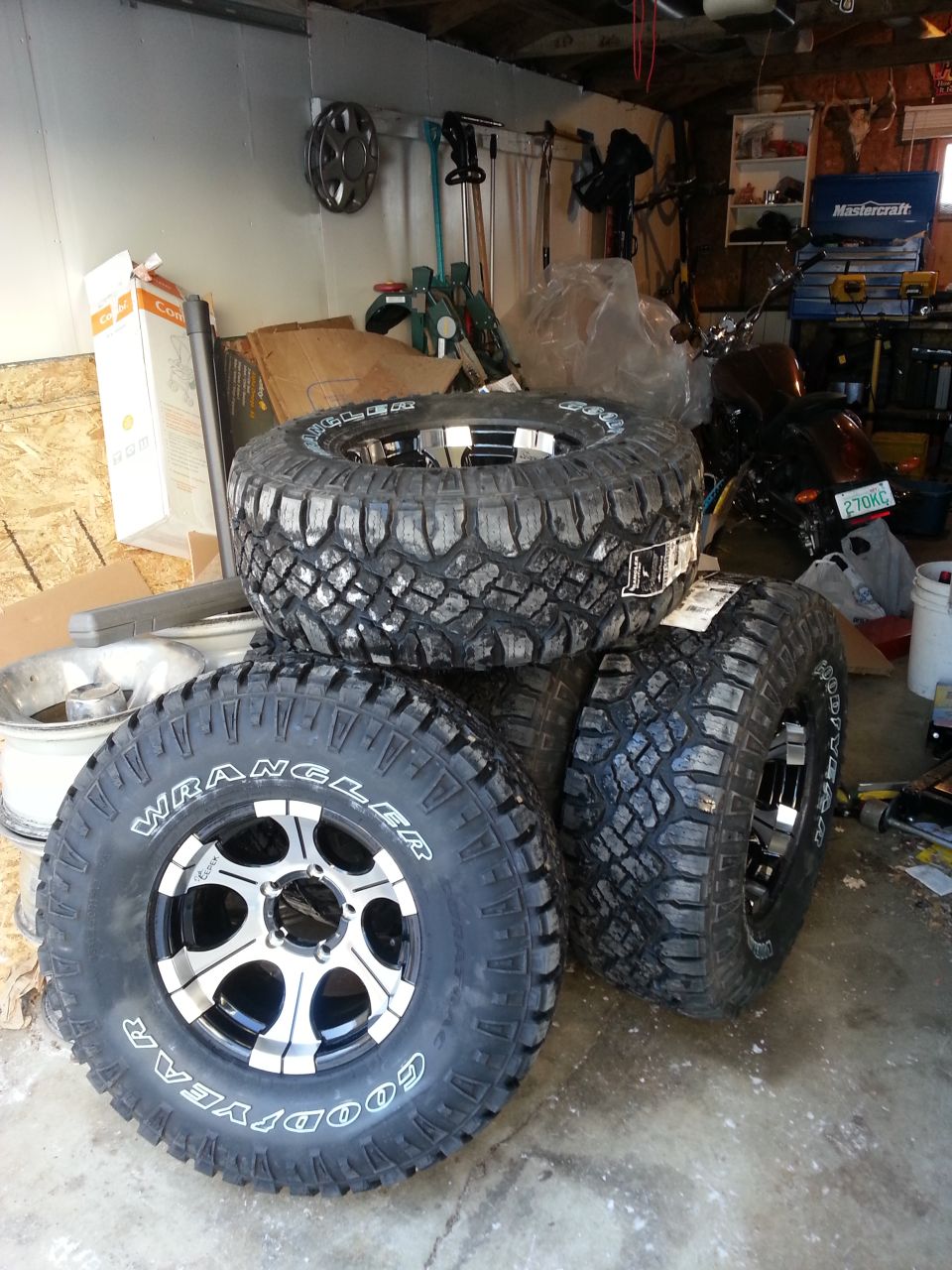 Four Goodyear Wrangler off-road tires mounted on chrome and black wheels stacked in a garage