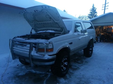 1994 Ford Bronco - A white Ford Bronco sits in the snow with its hood up, revealing the engine bay.