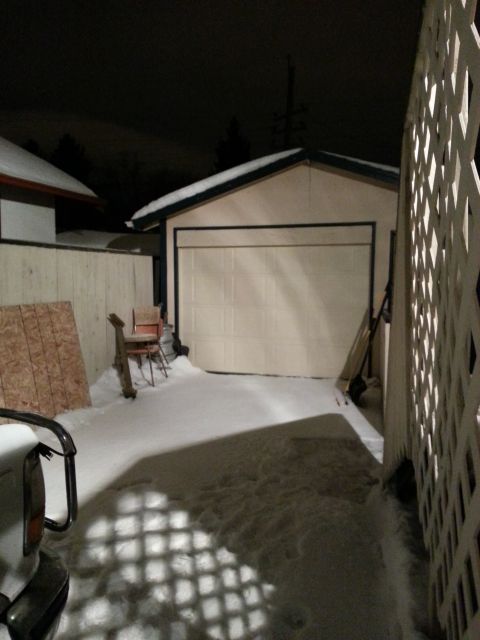 1994 Ford Bronco - A vehicle's rear corner is visible in a snowy driveway at night, next to a garage.