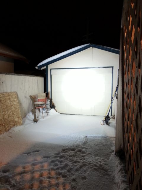 1994 Ford Bronco - A snow-covered driveway leads to a closed garage door, illuminated by a bright light, under a dark night sky.