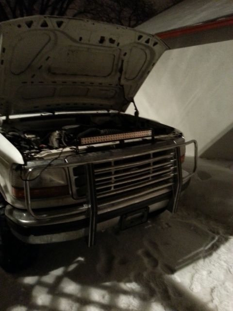 1994 Ford Bronco - The front of a white pickup truck is shown with its hood open, revealing the engine bay and an aftermarket light bar.