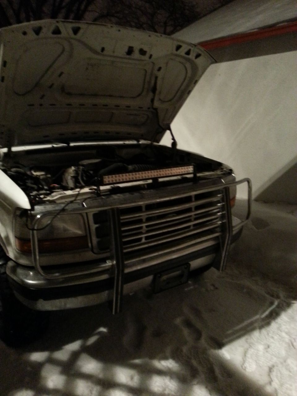 White pickup truck with hood up, showing engine and a light bar across the front