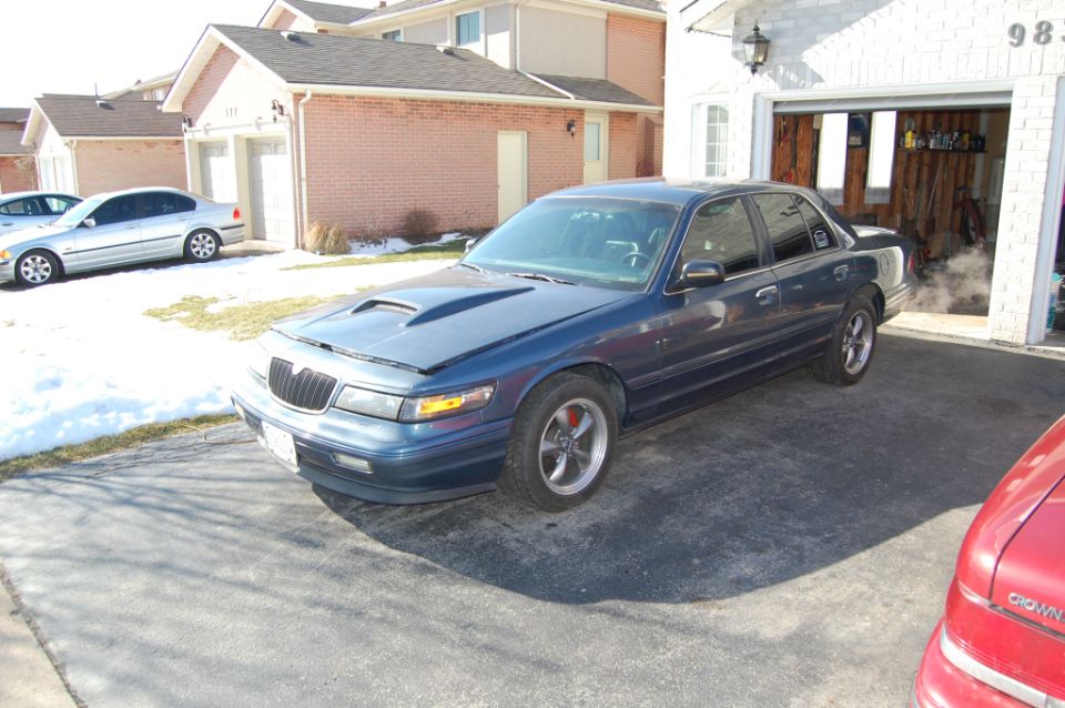 Blue sedan with hood scoop and aftermarket wheels parked in driveway