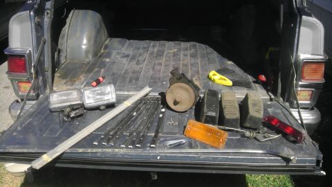 1982 Jeep Wagoneer - Tailgate of a 1982 Jeep Wagoneer open, displaying various disassembled parts including headlights and a taillight.