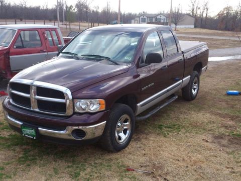 2004 Dodge 1500 - A maroon Dodge Ram pickup truck is parked on a grassy area with a second vehicle visible in the background.