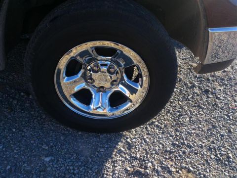 2004 Dodge 1500 - A close-up view of a chrome wheel and tire on a truck, parked on a gravel surface.