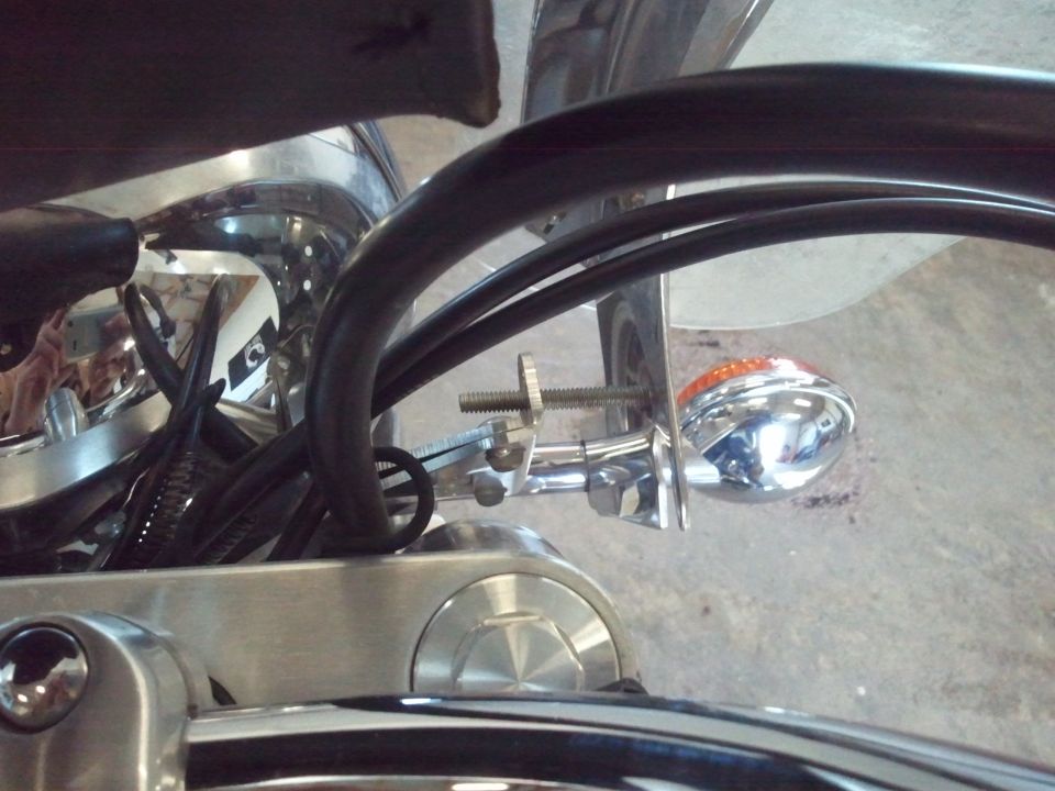 Close-up of a chrome motorcycle turn signal with an orange lens, attached to a black handlebar