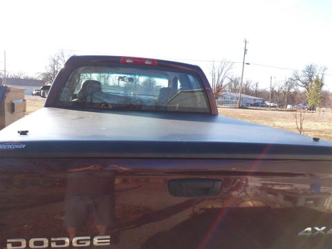2004 Dodge 1500 - Rear view of a red Dodge pickup truck equipped with a dark tonneau cover and "DODGE" badging visible on the tailgate.