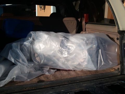 1994 Ford Bronco - The rear cargo area of a vehicle contains a large item covered in plastic wrap, with a Supermotors logo in the corner.