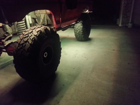 1978 Ford Bronco - Close-up of large off-road tires and suspension on a modified vehicle, with underglow lighting.